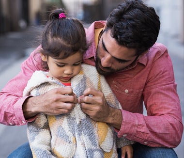 An adult helps a young child button a patterned coat